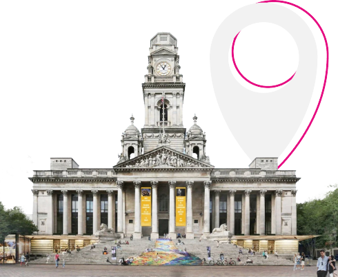 A neoclassical building with columns and a clock tower, featuring yellow banners and a rainbow-coloured ramp at the entrance, with a large pink location pin in the background.