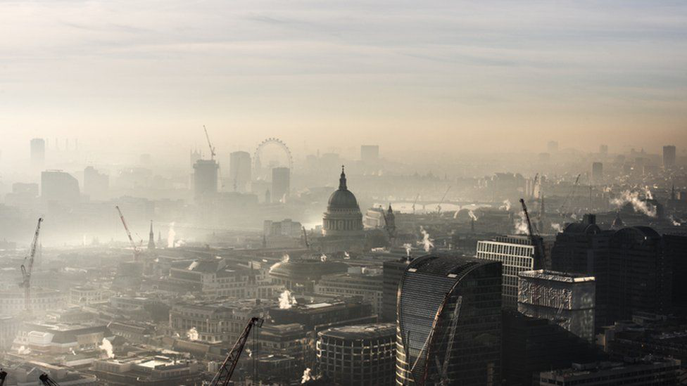 A hazy cityscape of London with visible air pollution, featuring St Paul’s Cathedral, construction cranes, and the London Eye in the background.