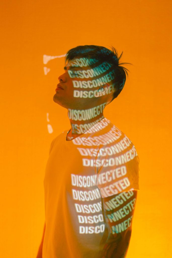 A person stands against an orange background with the words DISCONNECTED and CONNECTED projected across their face and body.