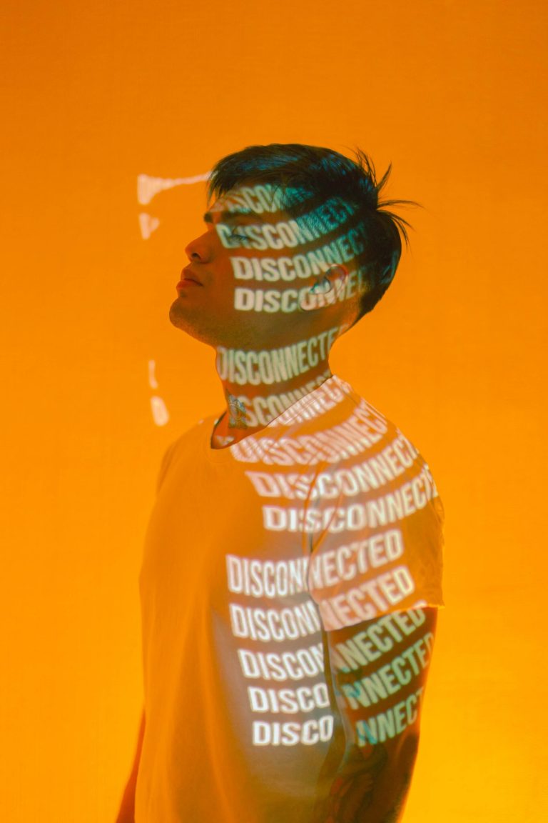 A person stands against an orange background with the words DISCONNECTED and CONNECTED projected across their face and body.