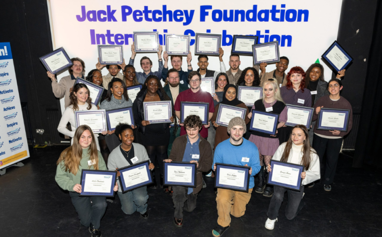 A group of people stand on stage holding framed certificates in front of a sign reading Jack Petchey Foundation Internship Celebration.