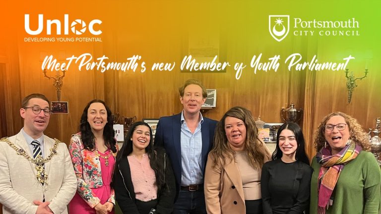 Seven people, including the Lord Mayor, stand smiling in front of wooden panelling under banners for Unloc and Portsmouth City Council, announcing Portsmouth’s new Member of Youth Parliament.