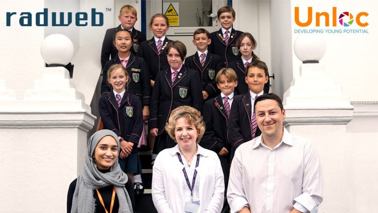 A group of schoolchildren in uniforms pose on steps with two women and one man in front. Logos for radweb and Unloc are visible in the top corners.