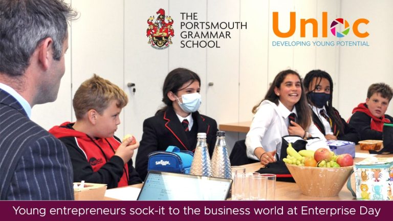 A group of students in school uniforms sit around a table with an adult, engaging in a discussion at Portsmouth Grammar School’s Enterprise Day event.